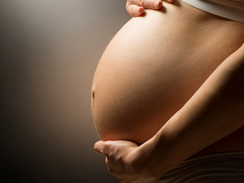 a imagem ilustra a barriga de uma pessoa grávida, que está com as duas mãos na barriga